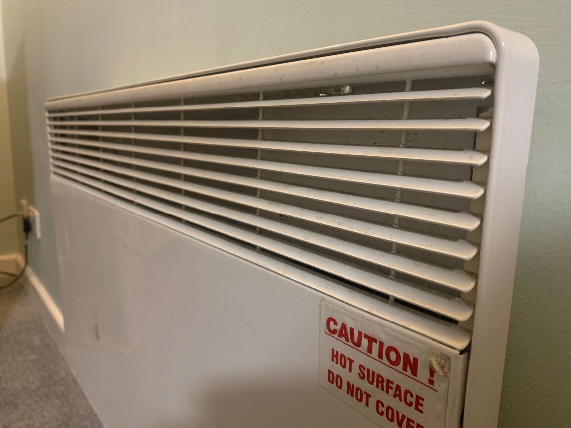 A wall-mounted electric heater featuring a prominent "Caution: Hot Surface" warning label.