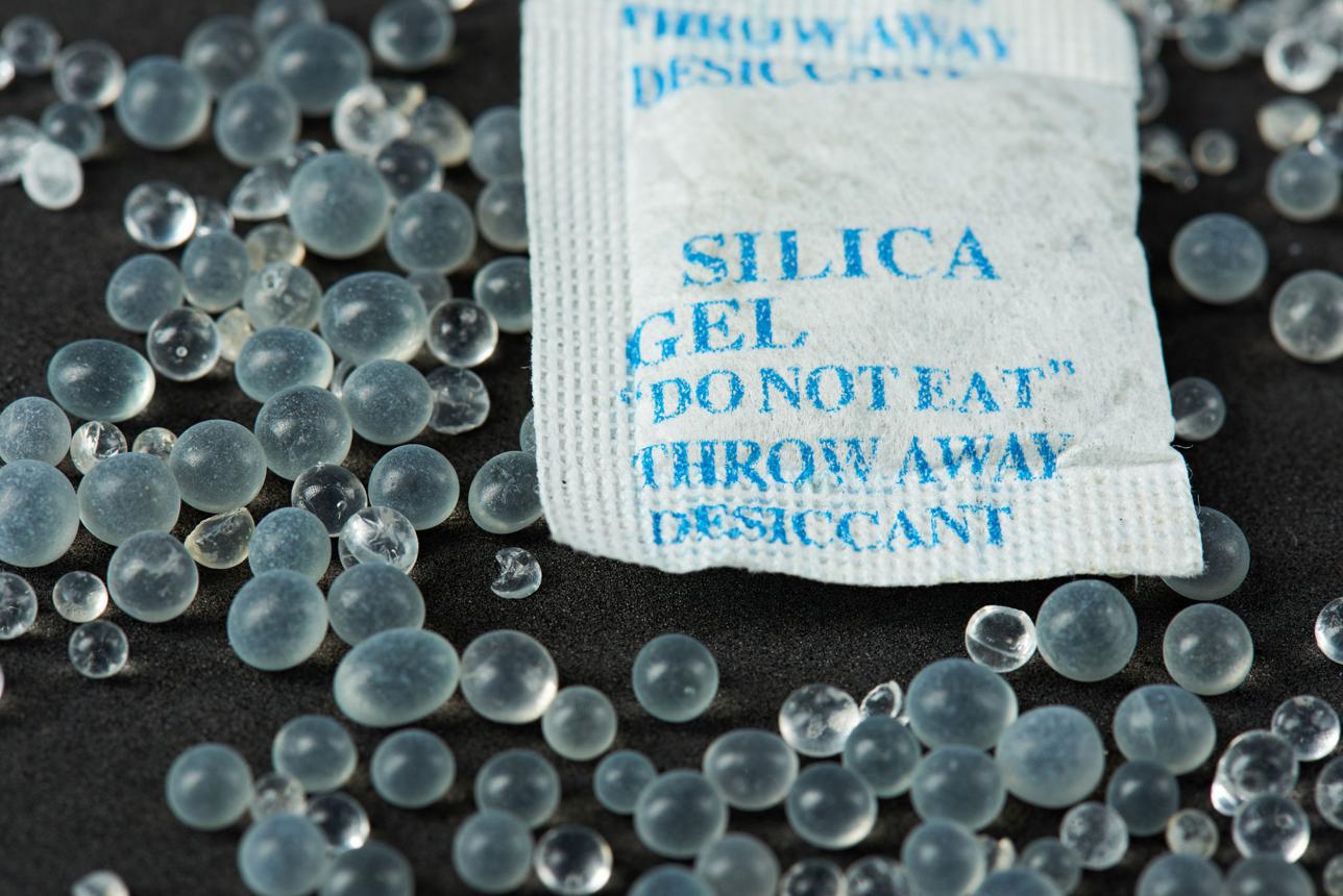 Close-up of translucent silica gel beads scattered around a desiccant packet to prevent moisture damage.