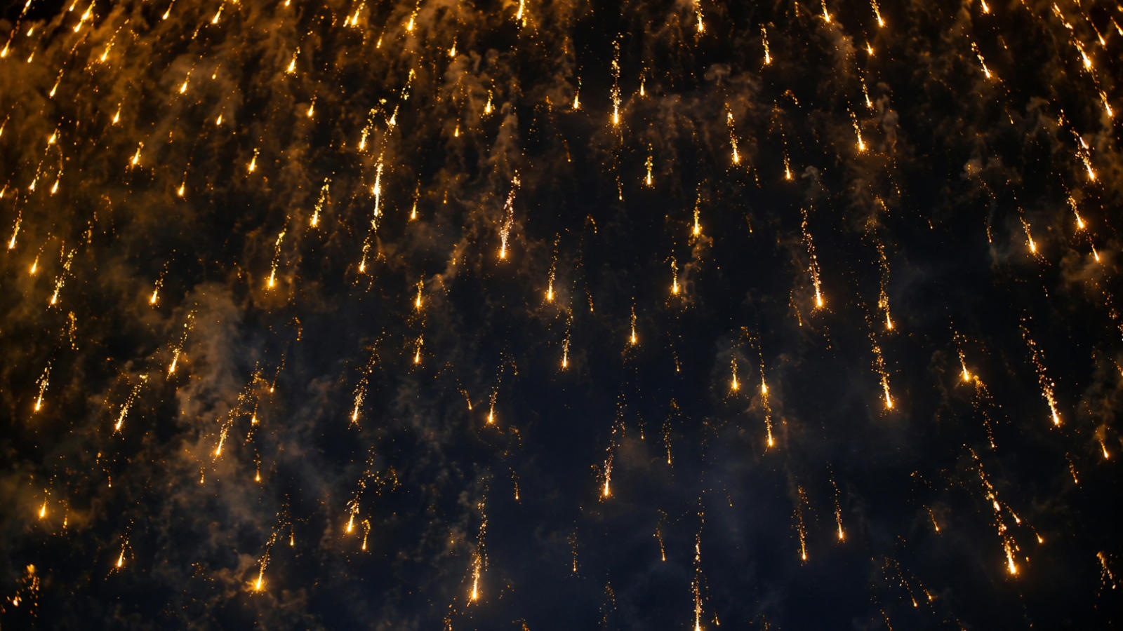 Golden falling leaves specialty fuse drifting slowly downward like a glowing, gentle cascade of light against smoke and dark sky.