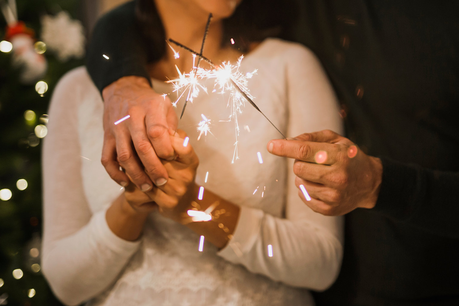Close-up of a bride and groom embracing while holding two lit burning sparklers together.