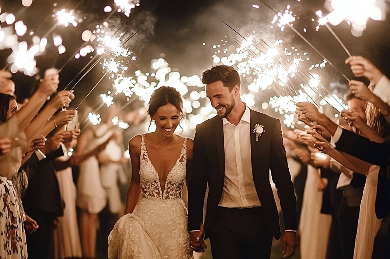 Bride and groom holding hands and smiling while walking through a bright tunnel of wedding send-off sparklers lit by guests.